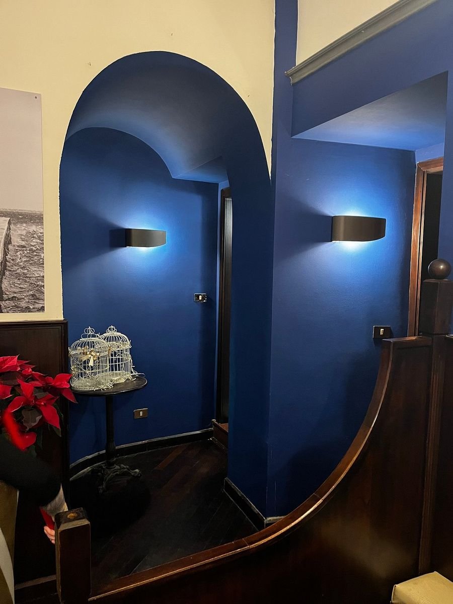 Interno del New Circus a Trieste: parete blu, lavagna dei drink e grande stampa in bianco e nero della città